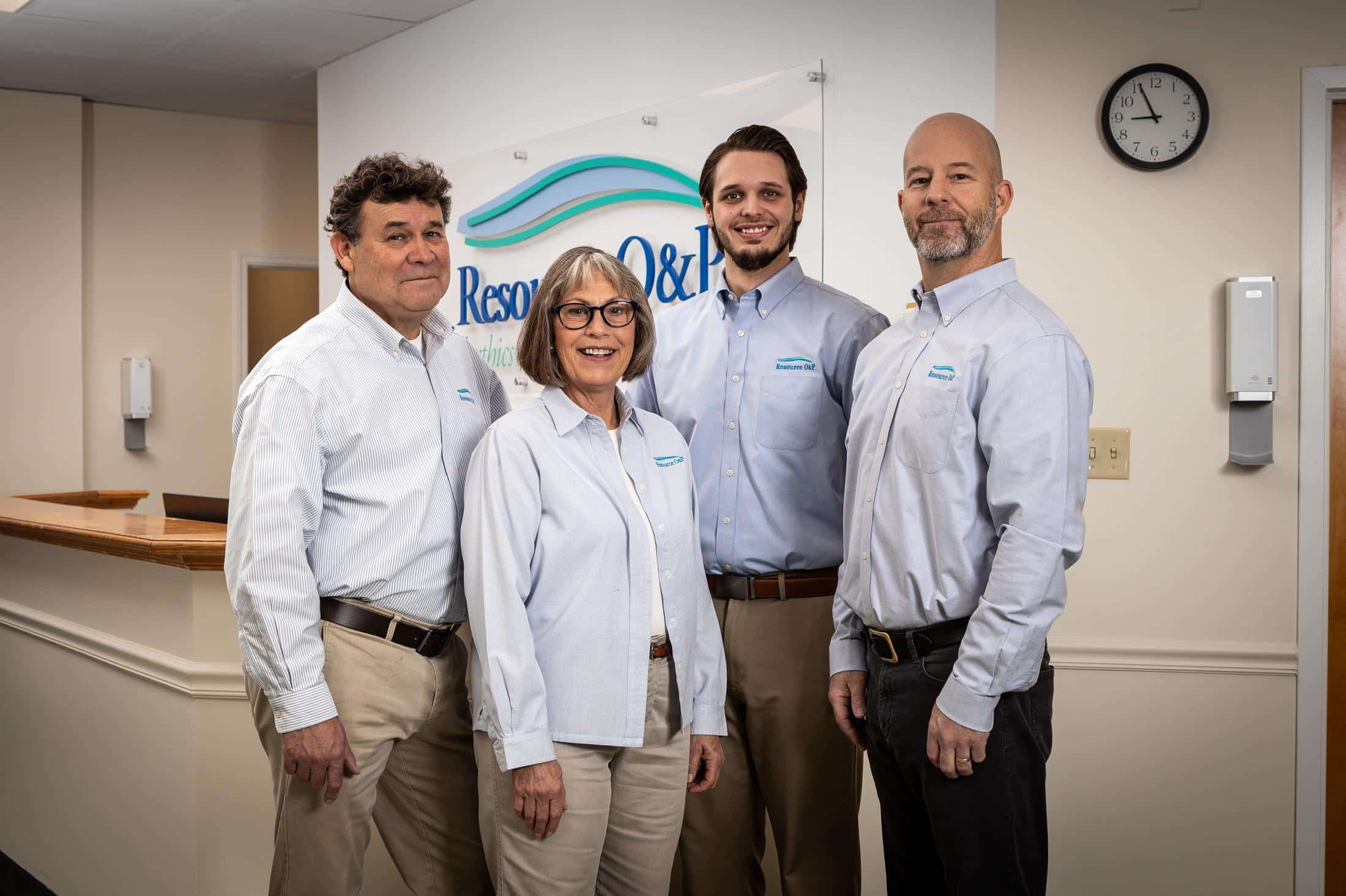 The four members of Resource O&P standing in front of the sign at the front desk of the office.